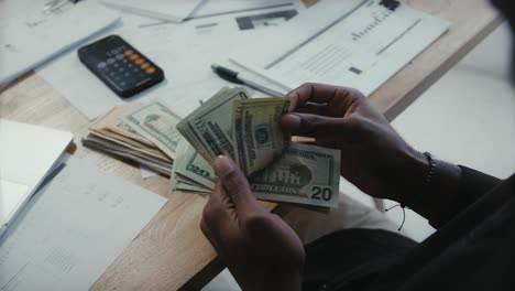 close up of man's hand counting money and making expense budget for the month sitting in his office desk with charts and calculator, money financial management concept