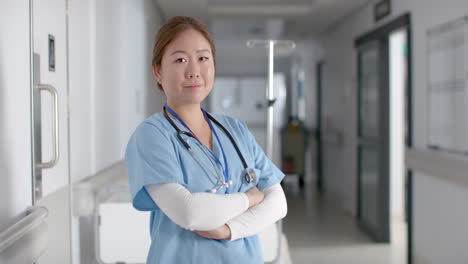 portrait of happy asian female doctor wearing scrubs in hospital corridor, slow motion