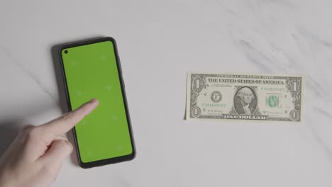 overhead currency shot of us 1 dollar bill next to person using green screen mobile phone