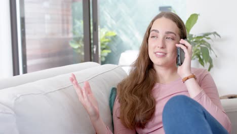 mujer caucásica feliz acostada en el sofá y hablando en el teléfono inteligente en cámara lenta