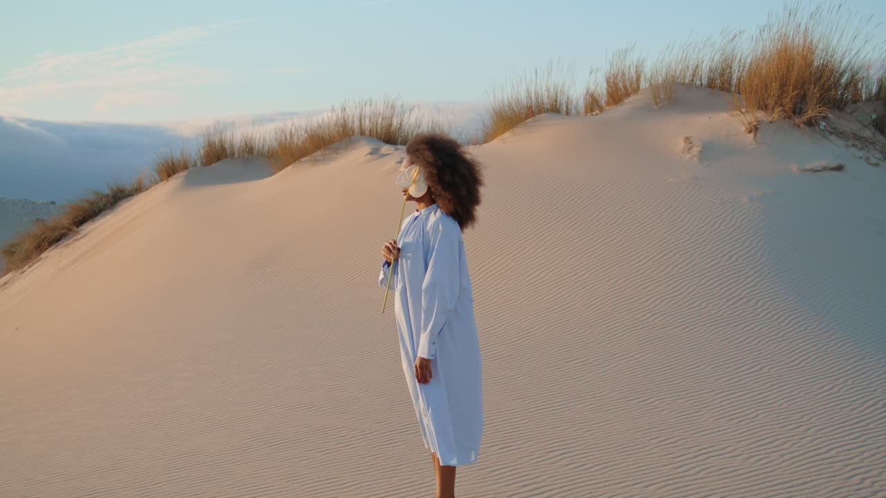 mujer sosteniendo una flor en el desierto de arena de verano. chica tranquila escondiendo la cara detrás de calla