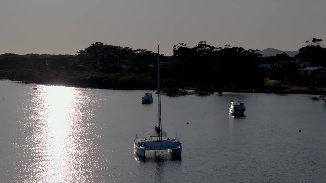 a group of boats floating on top of a lake next to a forest covered hillside and a town in the distance