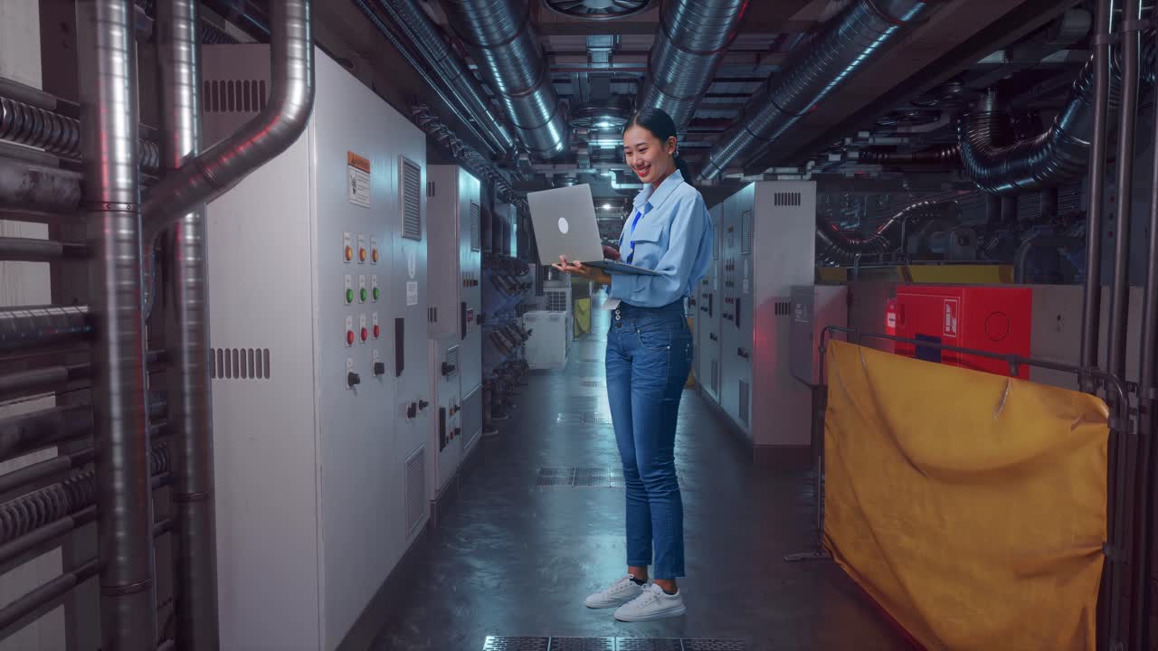 Full Body Side View Of An Asian Female Professional Worker Standing With Her Laptop In Engine Control Room, Typing On Her Laptop'S Keybaord With Meditation