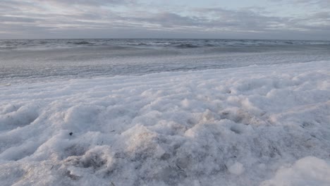 Ice-covered-sea-waves-rolling-in-on-beach