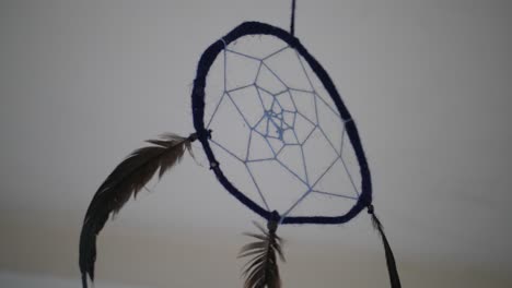 a close up of a dreamcatcher inside a dark, abandoned room with a simple white backgorund and ceiling