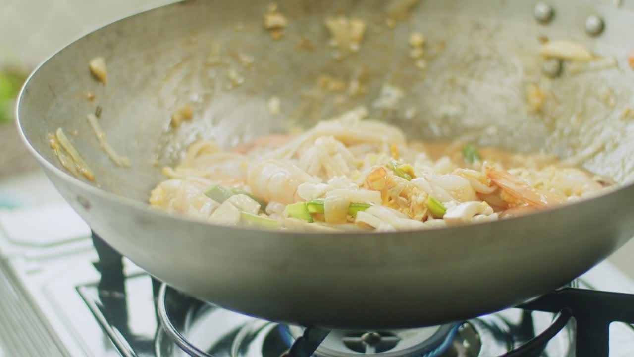 Donna che mescola noodles caldi nel wok con le bacchette.
