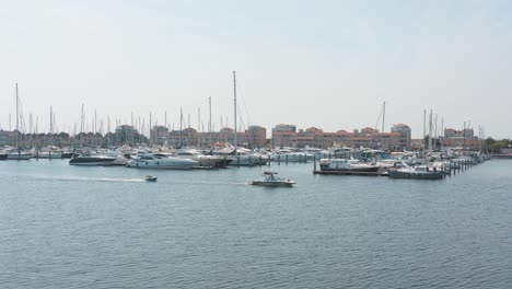 Cinematic-drone---aerial-shot-of-two-boats-on-a-marina-in-the-background-with-sailing-boats-on-a-sunny-day,-25p