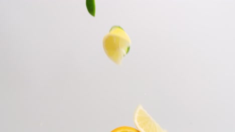 lemon, lime and orange citrus wedges and slices falling in slow motion on white backdrop