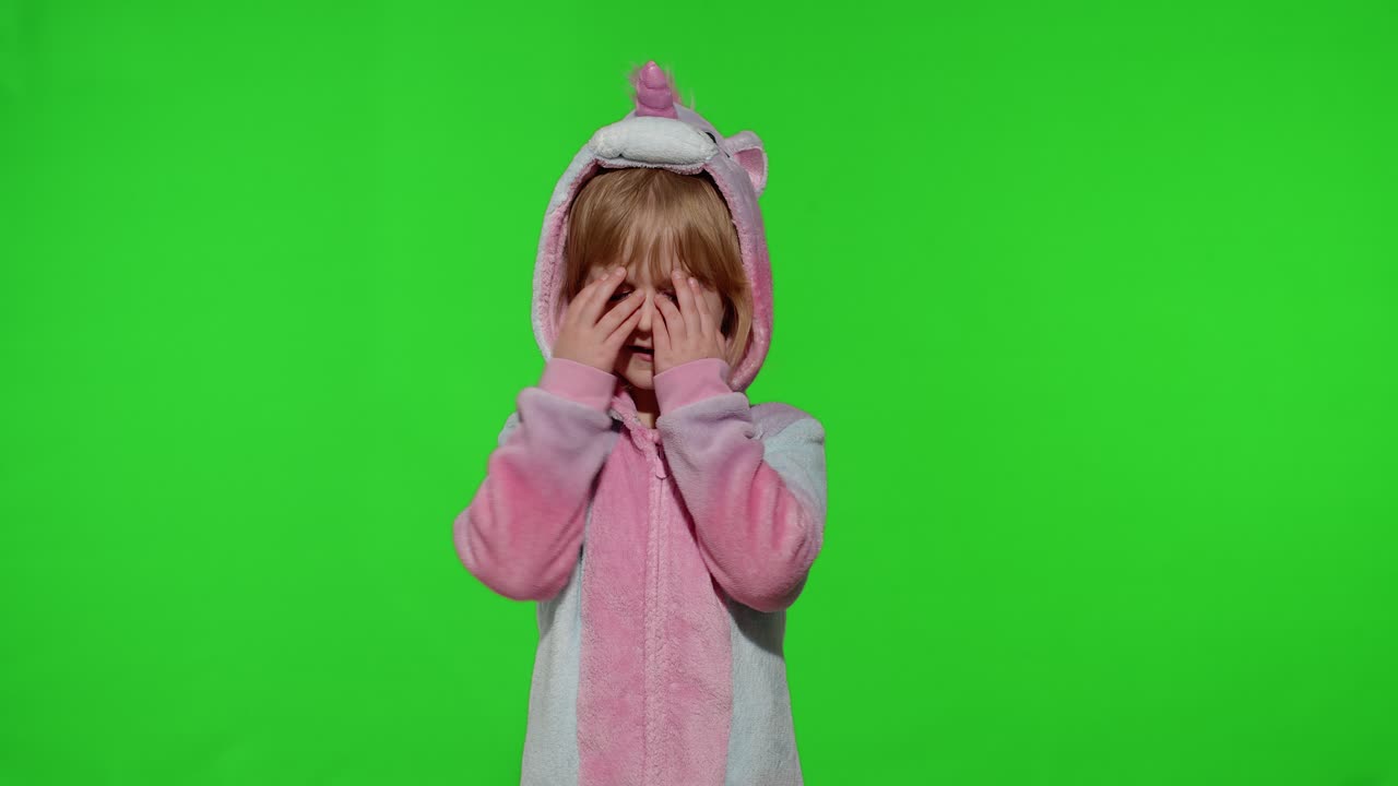 Little blonde child in unicorn costume crying, wiping tears with her hands on chroma key background