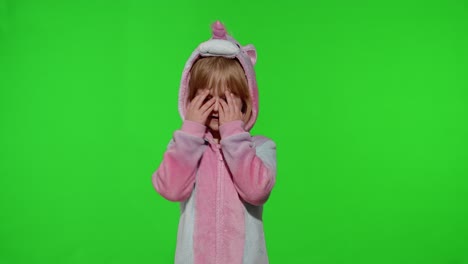 little blonde child in unicorn costume crying, wiping tears with her hands on chroma key background