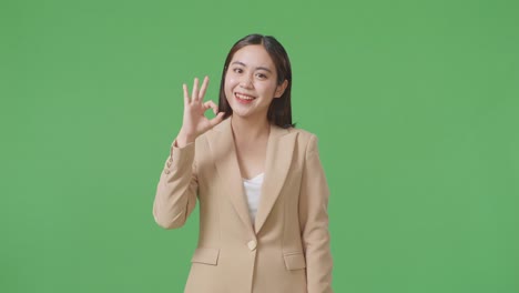 an asian business woman showing ok gesture and smiling while standing in the green screen studio