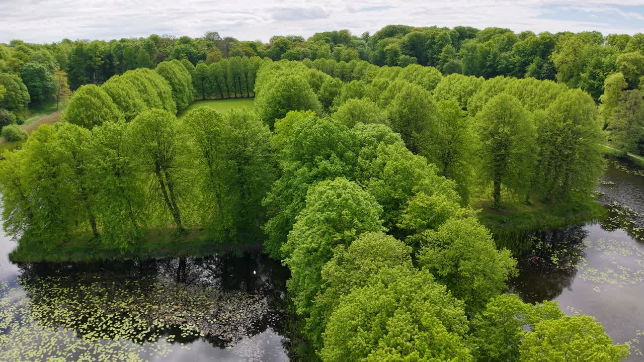 Drone view of lush green trees surrounding the reflective pond in the gardens near Hørsholm Church, Denmark