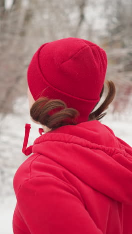 young adult wearing red beanie and hoodie jogging through snow covered park pathway flanked by evergreen pines under foggy winter sky embodying fitness and determination outdoors morning