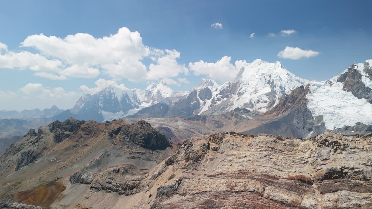 Sweeping aerial panning shot showcases the iconic, snow-capped Cordillera Huayhuash mountains and rugged valleys, highlighting Peru’s world-renowned high-altitude trekking route