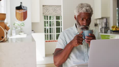 African-american-senior-man-drinking-coffee-and-using-laptop