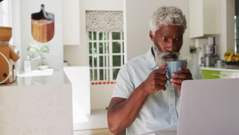 hombre mayor afroamericano bebiendo café y usando una computadora portátil