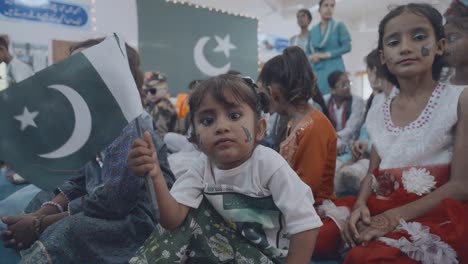 children sitting in a hall celebrating independence day in pakistan, joyfully holding the national flag. a heartwarming scene capturing cultural pride and festive spirit.