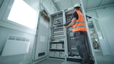 el ingeniero eléctrico que trabaja comprueba la tensión de corriente eléctrica y la sobrecarga en la parte delantera del gabinete del centro de carga o de la unidad de consumo para el mantenimiento en la sala principal del sistema de distribución de energía.
