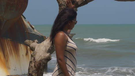 A-model-captivated-by-the-waves-crashing-on-the-shoreline-with-a-shipwreck-in-the-background