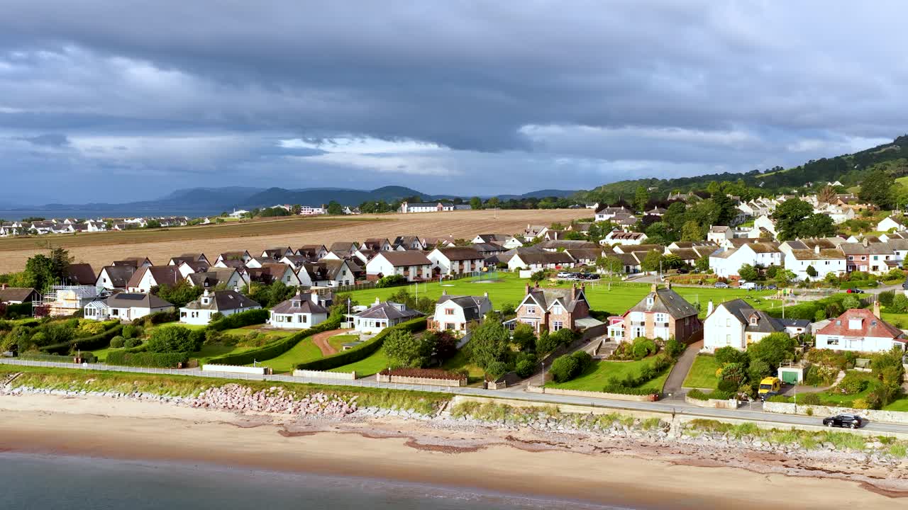 Drone camera smoothly pans above Rosemarkie village, beachfront houses, and scenic Scottish coastline