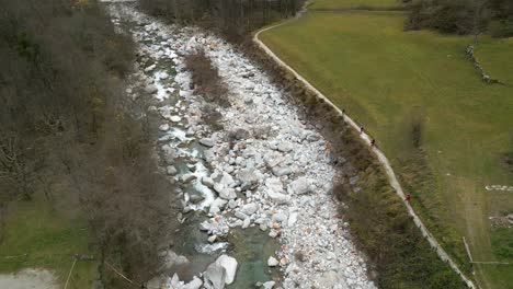 Drone-flying-above-the-crsytal-clear-glacial-waters-of-River-Maggia,-running-along-the-village-in-Cavergno,-in-the-district-of-Vallemaggia,-in-the-canton-of-Ticino-in-Switzerland