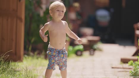 a little fair-haired bare-chested boy with his diaper sticking out of his shorts runs happily in the yard