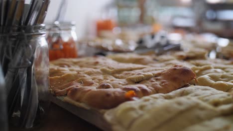 primer plano de un buffet mediterráneo con pan de pita y focaccia en primer plano y cubiertos al lado con palitos de zanahoria y más pan en el fondo