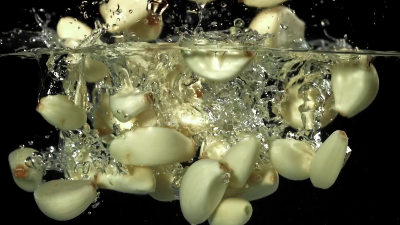 Gousses d'ail fraîches tombant dans l'eau avec des éclaboussures au ralenti