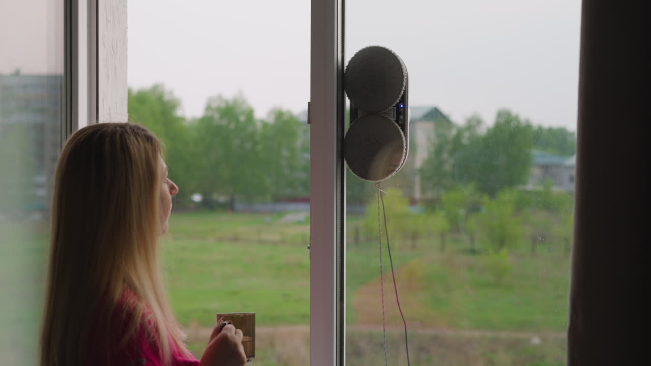 여자는 자동 로 ⁇  창기 청소기를 제어하기 위해 리모컨을 사용합니다.