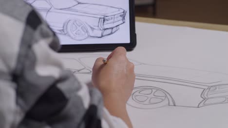 close up of male's hands drawing new car concept on paper following by photo on tablet on the table in the studio