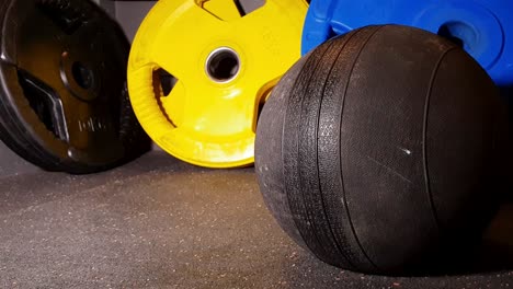 weight-med-ball-hitting-the-rubber-floor-at-strength-gym-with-colored-weights-in-the-background,-cinematic-slider