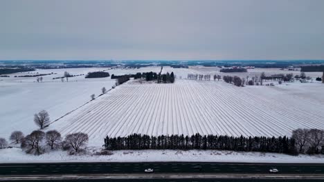 canada highway 401 in winter, with farm in background with snow covered field and cars and truck traveling