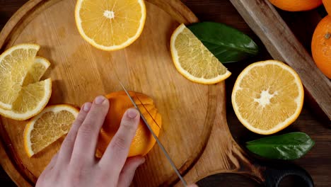 las manos de los hombres cortan naranjas maduras en una tabla de cortar.