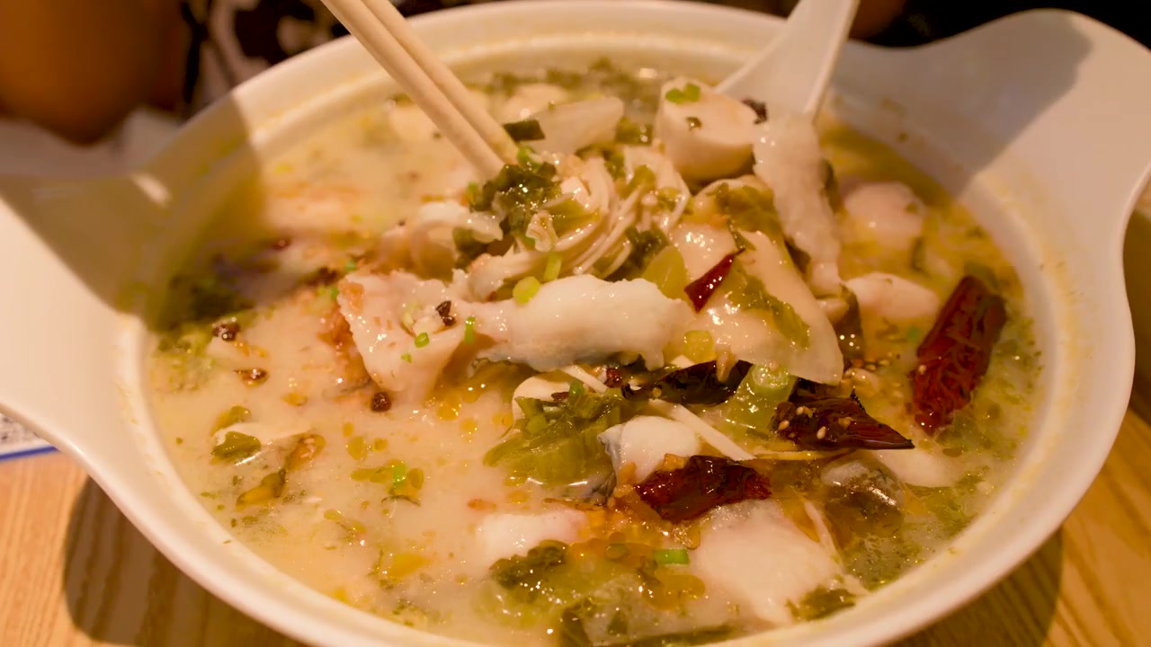 Persona comiendo sopa de pescado picante con palillos y cuchara