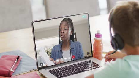 Composition-of-caucasian-schoolboy-on-laptop-online-learning-with-african-american-female-teacher