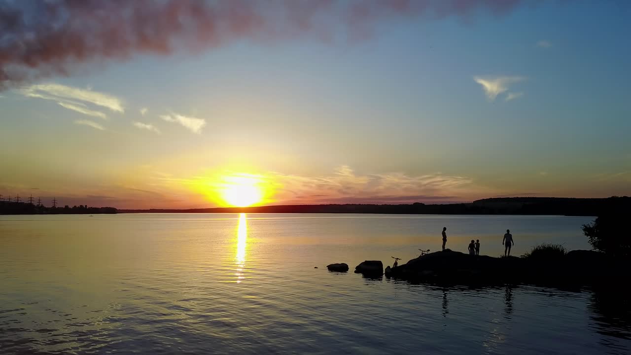 People Near Power Station. People near plant with pipes standing on the banks of the river at evening