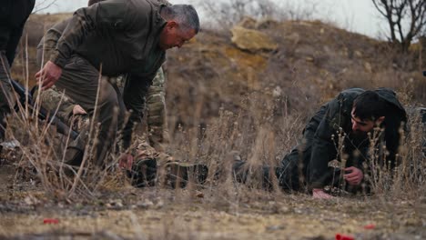 cuatro hombres confiados soldados experimentados llevan un soldado herido en un uniforme de camuflaje y un hombre moreno en ropa verde oscuro tropieza dejando caer a un soldado ferido durante la lucha en la estepa