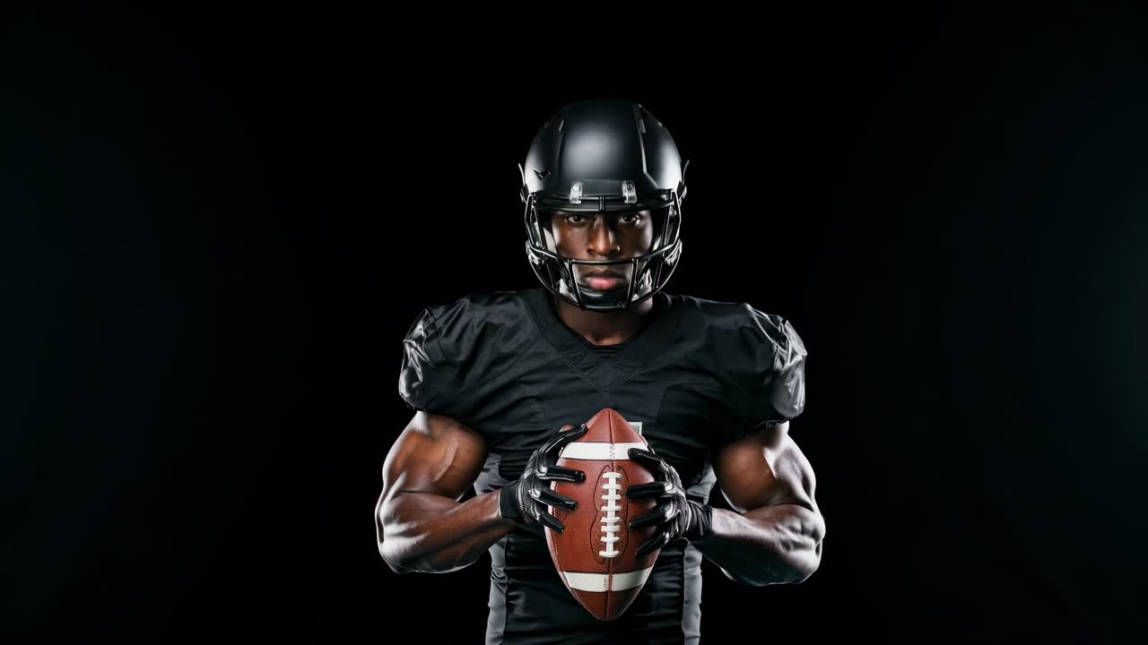Un'immagine drammatica dal basso di un giocatore di football americano con divisa nera che tiene in mano un pallone, sullo sfondo scuro