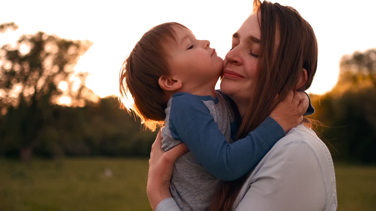 Il figlio bacia la madre seduta in un campo al tramonto, abbracciandola con amore. Festa della mamma.