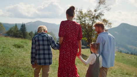 familie verbringt urlaub auf der wiese an einem sonnigen tag. eltern spazieren mit ihren kindern durch das gras.