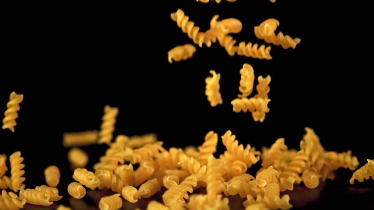 Massa Fusilli Seca Caindo em Câmera Lenta sobre uma Superfície Preta
