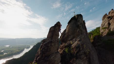 Un-Tipo-Sube-A-La-Cresta-De-Una-Montaña,-El-Sol-Brilla-Detrás-De-él-Mientras-Se-Para-En-La-Cima-De-La-Montaña,-Sobre-El-Horizonte-Movimiento-Aéreo-Dinámico-De-Drones-Fpv,-Velocidad-Rápida,-Búlder-De-Habilidad,-Escalada-Libre-En-Solitario