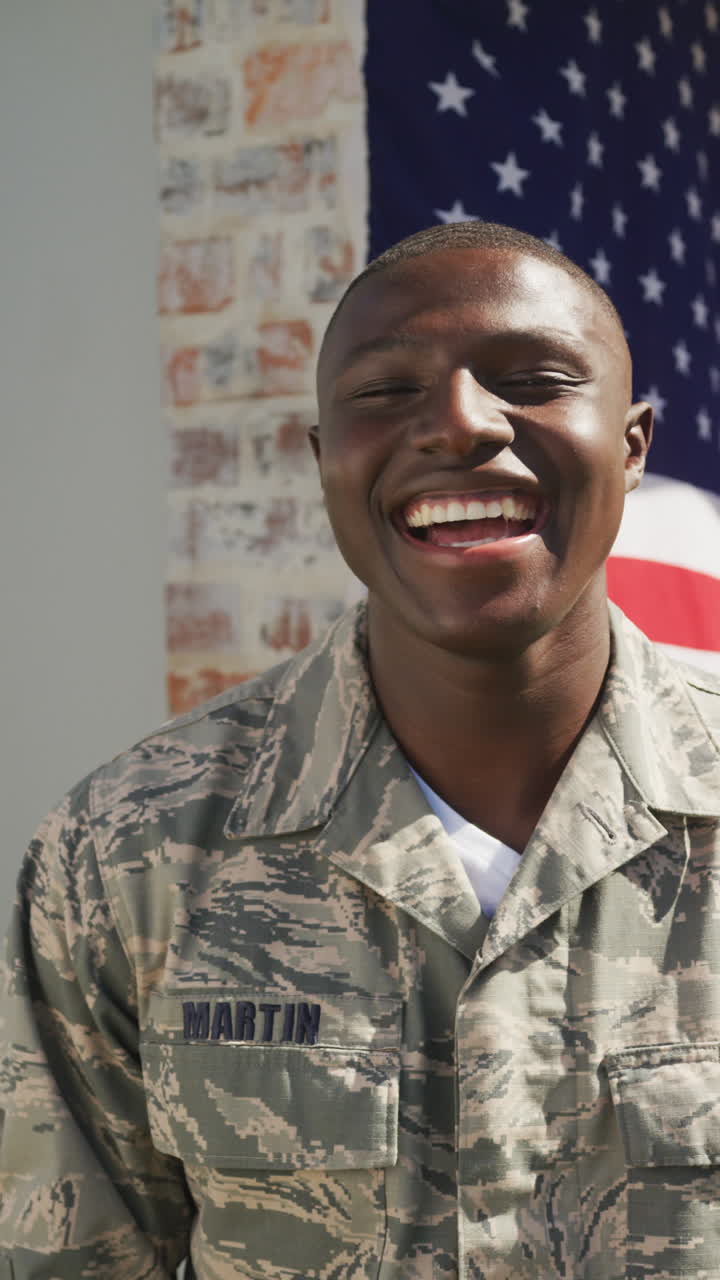 retrato de video vertical de un feliz soldado afroamericano en uniforme frente a la bandera estadounidense