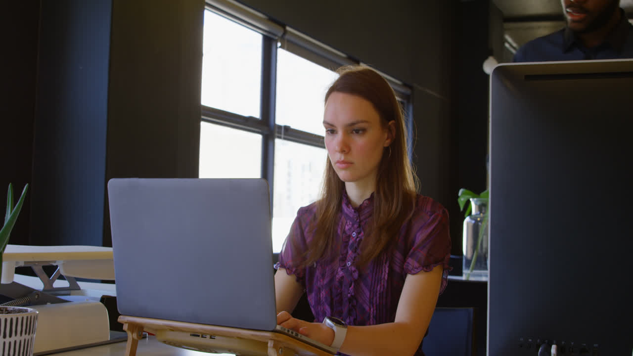 vista frontal de una joven mujer de negocios caucásica trabajando en una computadora portátil en un escritorio en una oficina moderna 4k