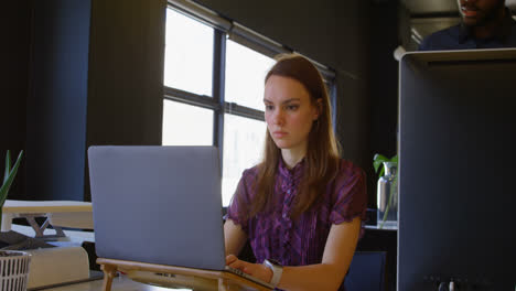 Front-view-of-young-caucasian-businesswoman-working-on-laptop-at-desk-in-a-modern-office-4k