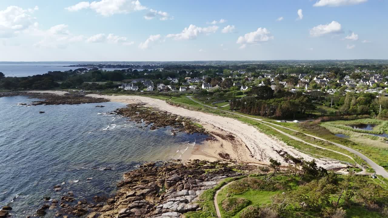 Una costa panoramica con una spiaggia, una costa rocciosa e case sullo sfondo, vista aerea