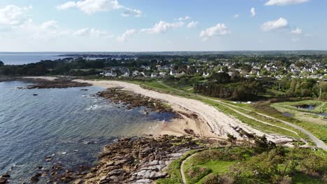 a scenic coastline with a beach, rocky shoreline, and houses in the background, aerial view