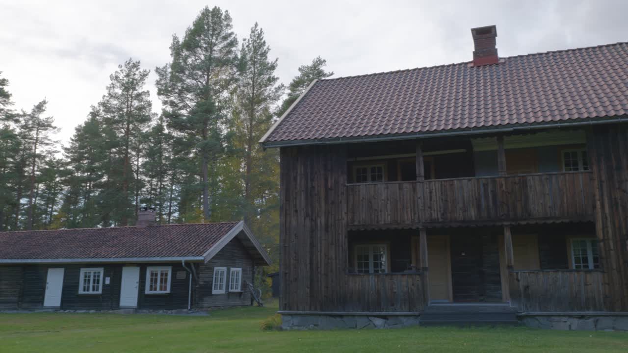 Pan shot of old wooden cottages nestled in a forest in Norway