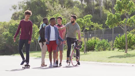 happy diverse male friends walking with bicycle and talking on sunny day