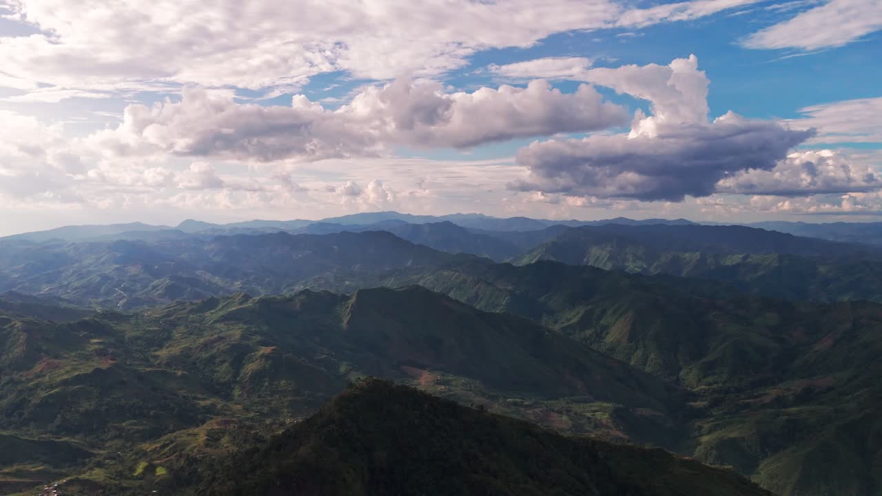 Cinematic 4K drone footage over a vast, layered mountain range in the Philippines. Rolling green hills recede to the horizon under a beautiful blue sky with fluffy white clouds